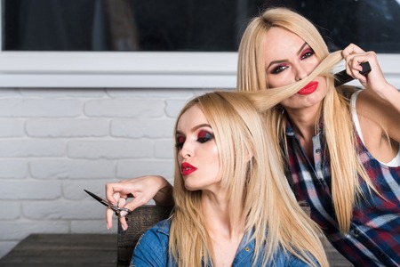 barbershop, scissors in hand of hairdresser works with blond hair of beautiful young woman or girl...