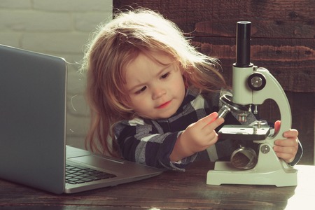 student boy with laptop and microscope study science at educational workplace makes experiment