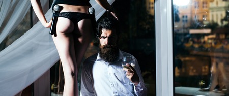 young couple of handsome bearded man hipster with long beard and pretty cute woman or girl with sexy legs and buttocks holding microphone or mic in restaurant with cocktail in glass near windowの写真素材