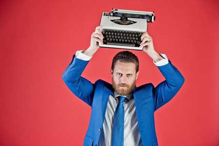 handsome man with typewriter in fashion business suit on red background with serious faceの写真素材