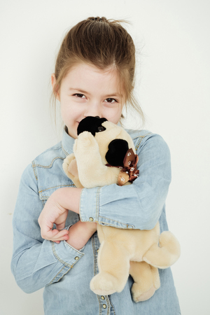 Happy, cute, small, little, girl, child in blue jean shirt cuddling adorable, soft toy dog or puppy isolated on white. Best friends. Love and friendshipの写真素材