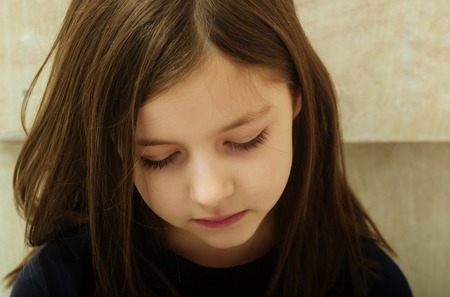 Sad cute, pretty, girl, child, kid with depress eyes on adorable face and long, brunette hair sitting on beige background. Loneliness, melancholy and boredomの写真素材