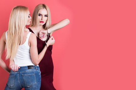 women in handcuff, fashion cloth posing on pink background, pretty blonde girl friends, twins sisters having bright makeup, homosexual and gay, copy spaceの写真素材