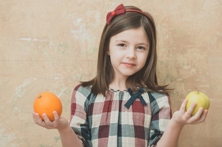 child or small, little girl with adorable face and long, brunette hair holding orange and yellow apple, natural, organic, vitamin fruit, in hands on beige wall. Healthy food and dietの写真素材