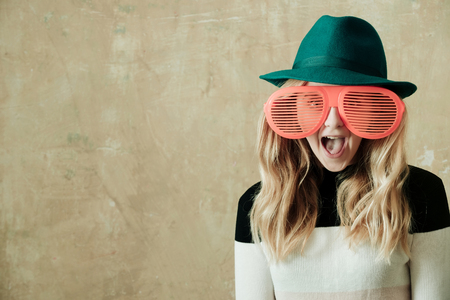 summer. cute fashion young happy girl posing with funny big orange glasses and green hat on beige background, copy spaceの写真素材