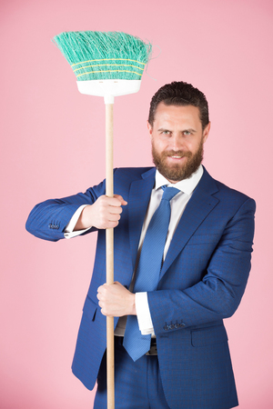 man or businessman with happy smiling face holding broom in blue formal suit or business outfit on pink background, pure businessの写真素材