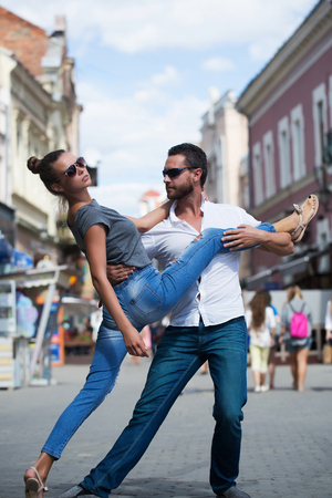 Dating, active lifestyle, vacation, pretty girl or cute woman and handsome man dancing on sunny, summer day on city street. Young, stylish, fashionable couple in love.の写真素材