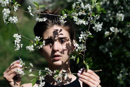 girl or cute woman with brunette hair holding frame of blossoming, white flowers in spring garden on...