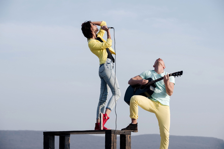 singer or girl singing on table and handsome man, guitarist playing acoustic guitar on sunny, summer day on blue sky. Young musicians performing on nature. Music concert and performanceの写真素材
