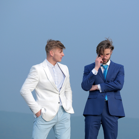 meeting and communication, partnership and team work, men speaking on mobile phone on blue sky background, businessman and employee in outfit outdoorの写真素材