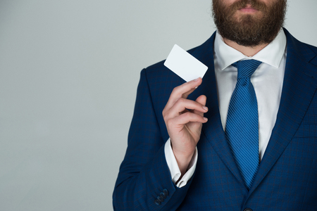 man holding white business card on grey wall background in blue formal outfit, copy spaceの写真素材