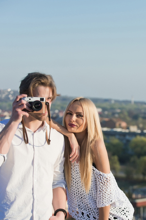 man or photographer looking through camera with pretty girl or sexy woman with long, blond hair on sunny day on natural background. Couple in love. Wanderlust. Idyllic summer vacationの写真素材