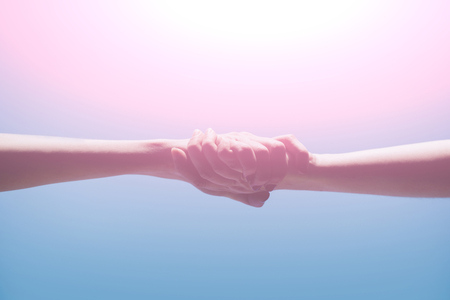 hands of women or girls holding strong together on bright, light, blue background. Grasp. Handshake....