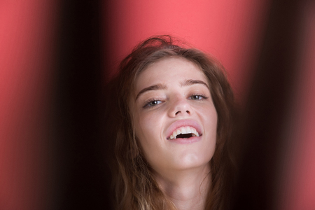 woman smiling with pretty smile, white, healthy teeth on young face, pure skin, no makeup and blond, long, wavy, hair on blurred black and red wall. Beauty and stomatologyの写真素材