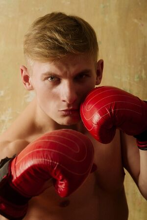 boxing gloves red color on hands of strong, fit, athletic man, boxer or athlete posing in stance with naked, muscle chest on beige background. Power, attack, defenceの写真素材