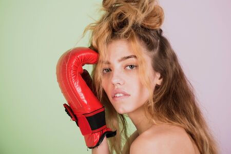 girl with red, boxing glove and blond, long, wavy hair, hairstyle, naked shoulders on violet and green wall. Natural beauty and sportの写真素材
