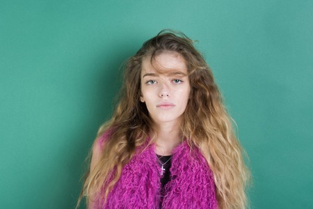woman or cute girl, stylish, young model with soft, blond, long, wavy, healthy hair, curly hairstyle posing in fashionable, pink feather boa on green wall. Natural beauty. Fashionの写真素材