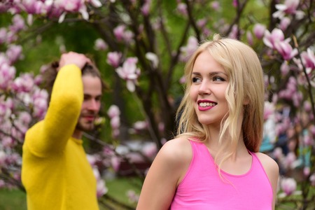 dating couple in love of smiling girl and man near pink magnolia flowers on tree in spring garden