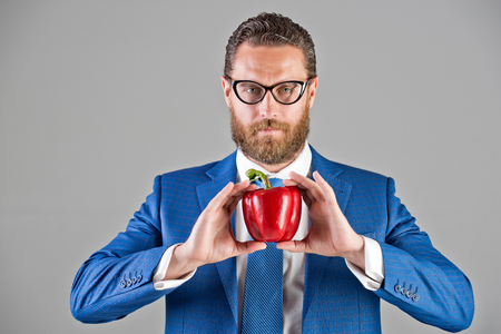 man in glasses or businessman holding red fresh vegetable of sweet pepper in blue outfit with serious confident face on grey background, healthy food and dietingの写真素材