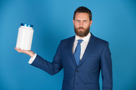 businessman or bearded man with plastic jar in formal outfit on blue background, copy space, moneybox, vitamin and drugの写真素材