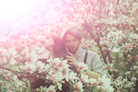 couple in love, man and pretty girl or cute woman enjoying pink, magnolia flower blossom on trees in flowering, spring park on idyllic, sunny day on blurred floral environment. Daydreamingの写真素材