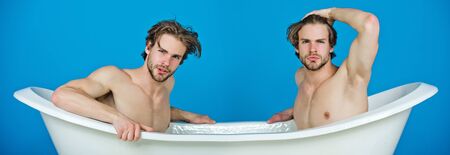 gay men or unshaven macho twins with stylish hair sitting naked, sexy muscular torso in white bath tub on blue background. Love and relationship, homosexual. Spa and hygieneの写真素材