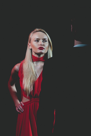 girl or pretty blonde woman in red dress and lip makeup, handsome man or businessman in outfit on black background, couple in loveの写真素材