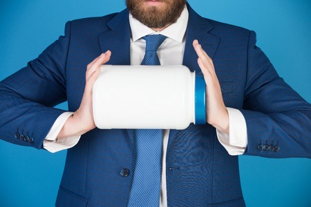 man holding jar for savings or sport nutrition, businessman in formal outfit on blue backgroundの写真素材
