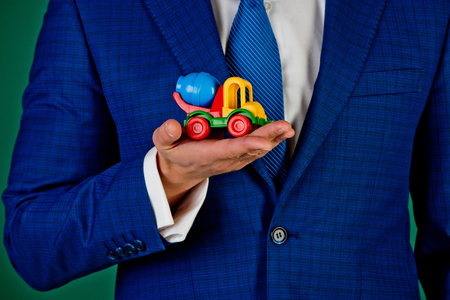 car in hand of man or businessman in blue outfit on green background, import and export, transportation, transit, colorful toy concrete mixerの写真素材