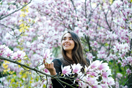 beauty and nature. Happy girl or pretty woman with long, brunette hair smiling at magnolia tree with...