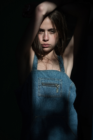 woman with brunette hair and no makeup in fashionable jeans denim dress blue color in sunlight on black background, beauty and fashionの写真素材