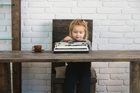 small boy or smiling businessman child sitting at table and typing typewriter with coffee cup on white brick wall background, business and new technologyの写真素材