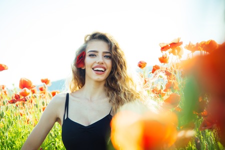 girl with long curly hair hold flower in field of red poppy seed with green stem on natural background, summer, spring, drug and love intoxication, opiumの写真素材