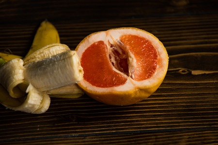 banana with yellow peel in red grapefruit on wooden backgroundの写真素材