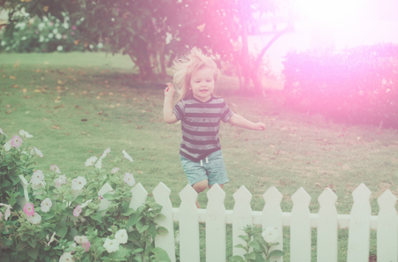 child. child or small boy outdoor in garden with flowers and green grass near white wooden fence hold mobile phone on natural background, summer vacation, childhood and happinessの写真素材