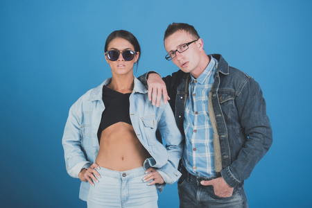 couple of stylish woman and man in sunglasses, glasses and jeans jacket on blue background, denim style, beauty and fashion, summer, couple in love, student lifestyleの写真素材