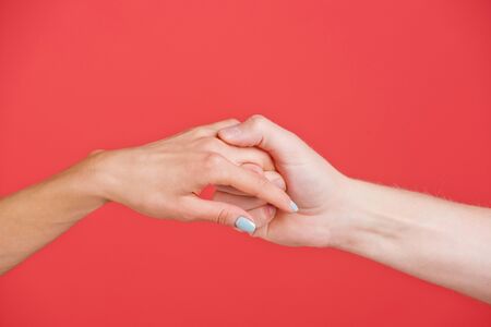 hands of man and woman hold each other on red background, help and faithの写真素材