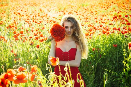 poppy seed bouquet at girl with long curly hair in red dress in flower field with green stem on natural background, summer, spring, drug and love intoxication, opiumの写真素材