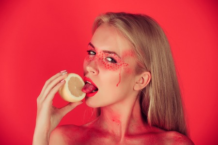 lemon in hand of woman with creative fashionable makeup on face hold and lick fruit in hands on red background, beauty and fashion, allergy, healthcare, vitamin, vegetarian and dietingの写真素材
