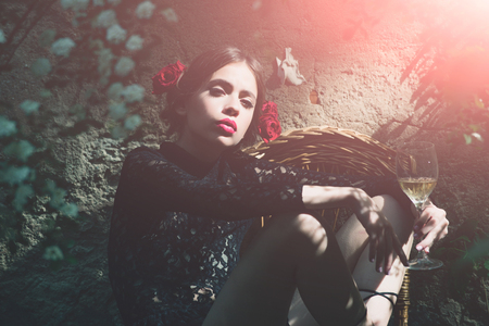 woman or cute girl, fashion model with red lips, makeup and wine glass sitting on wicker chair in yard on outdoor wall. Alcohol drinking. Enjoying life. Holiday celebration. Spring, summerの写真素材