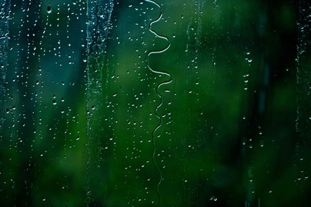 water drops on wet glass of window on blurred green backgroundの写真素材