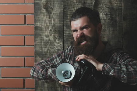 lamp with light bulb at angry brutal man or caucasian bearded hipster with long beard and moustache on grey wooden and red brick wall. Electricity and lightning. Idea and innovationの写真素材