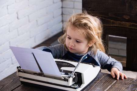 boy or small kid with typewriter and paper working at tableの写真素材