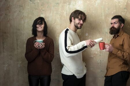 Smiling man pouring drink from bottle to cups of hipster with beard and adorable woman or cute girl. Happy friends drinking milk or yogurt on beige background. Healthy dieting and lifestyleの写真素材