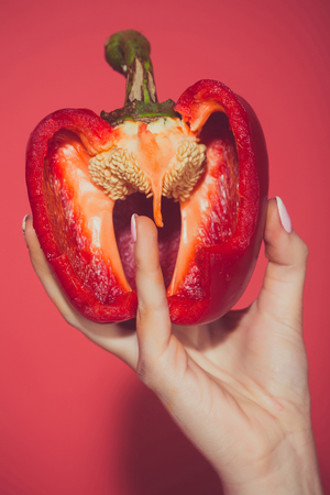 half of bell pepper in hand of woman hold sweet paprika on red background, healthcare and vitamin,...