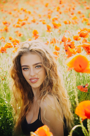 poppy seed. happy girl with long curly hair in red flower field with green stem on natural background, summer, spring, drug and love intoxication, opiumの写真素材