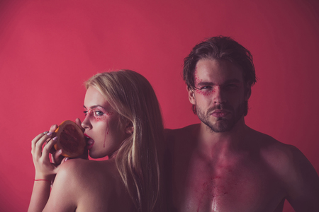 grapefruit at girl and man with creative fashionable makeup on face hold grapefruit fruit on red background, beauty and fashion, allergy, healthcare and vitamin, vegetarian and dieting, couple in loveの写真素材