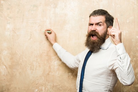 marketing planning of bearded man with long beard and hair on shouting face in tie and white shirt write on beige wall background with chalk and raised finger, copy space, business and marketing, educationの写真素材