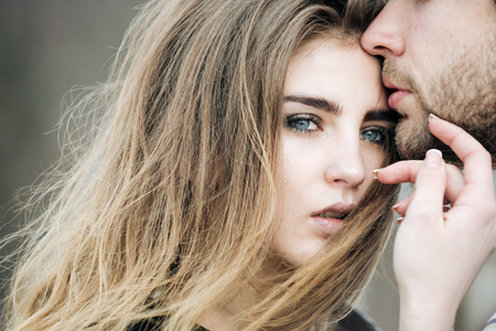 Sexy male lips with unshaven beard and moustache touching cute face of beautiful woman or pretty girl with fashion makeup and stylish long hair on natural background. Love and tendernessの写真素材
