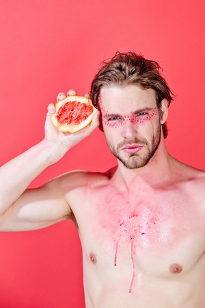 guy with creative fashionable makeup on face hold grapefruit fruit in hand on red background, beauty and fashion, allergy, healthcare and vitamin, vegetarian and dietingの写真素材